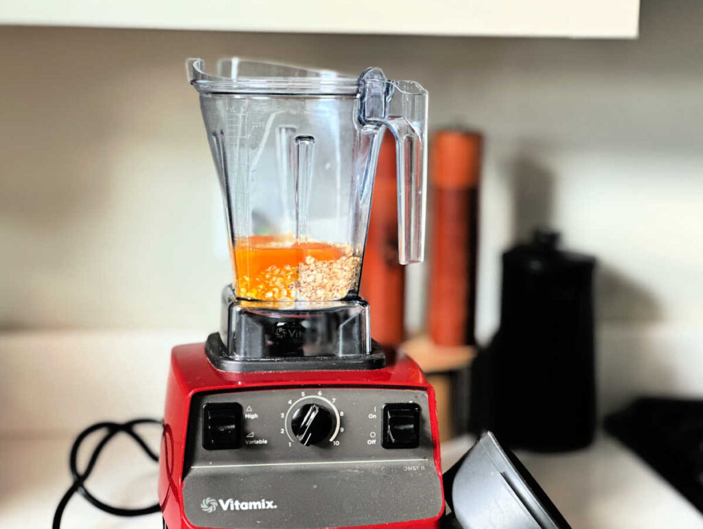 eggs, oats and cottage cheese in a red Vitamin blender on a kitchen countertop with salt and pepper shakers in the background and a French press coffee maker